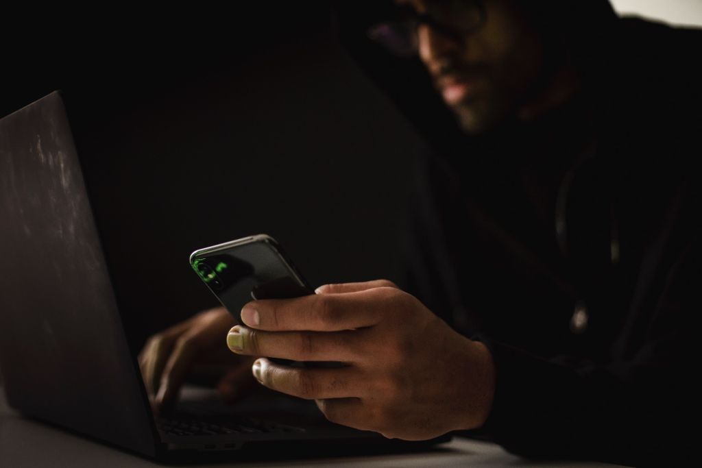 a fraudster with a smartphone typing on a laptop